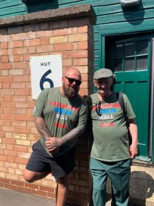 Two veterans wearing operation Berlin Wall t-shirts outside a hut