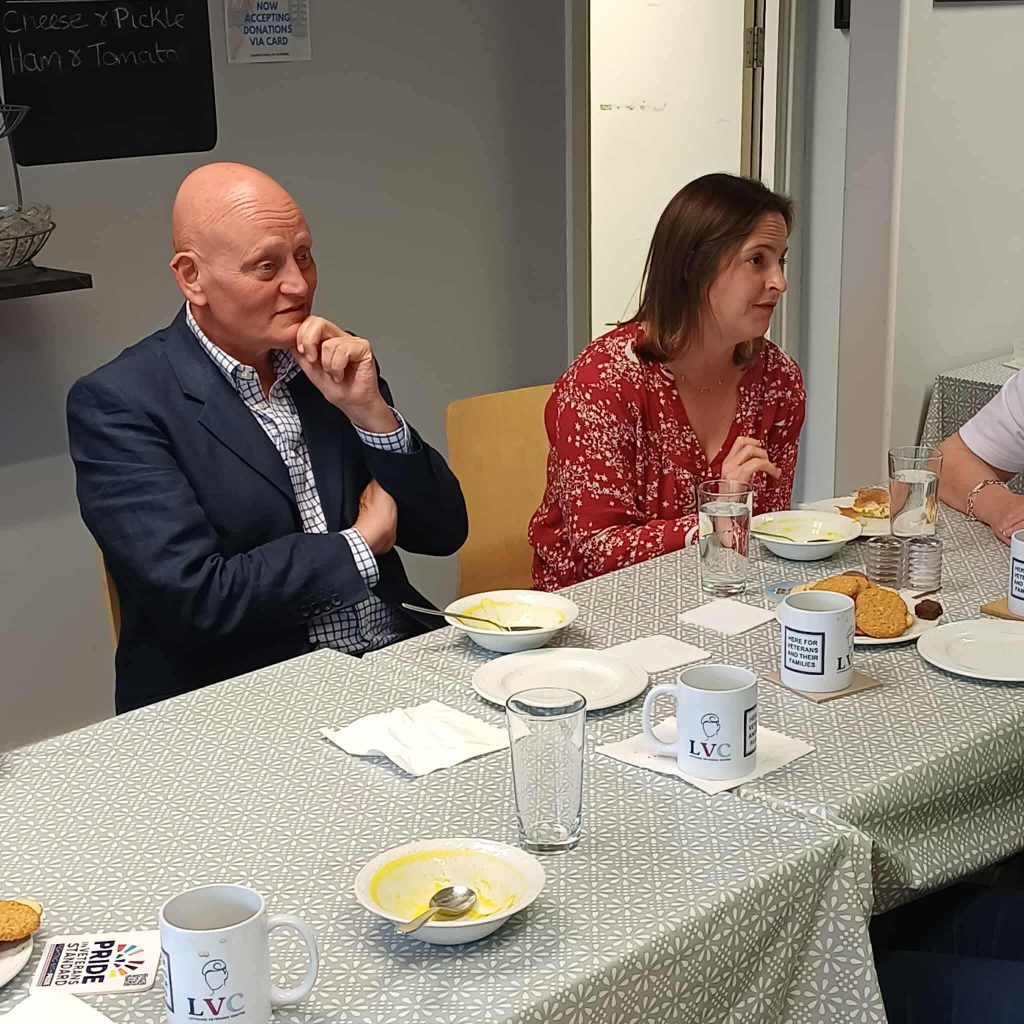 Major General (Retd) Tim Hyams sits at a table in the centre with a female during a visit