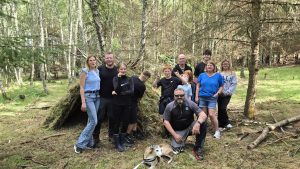 A group of Veterans and their families pose in front of a make shift hut