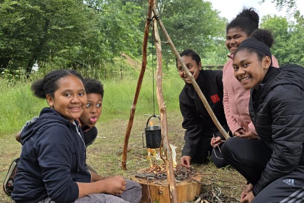 A group of children gathered around a campfire pulling faces