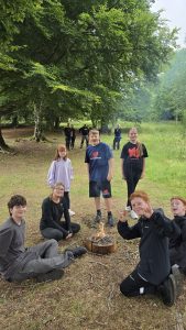 A group of veterans children posing whilst sat and stood around a small fire. Adults in the background watching on.