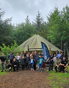 A group of veterans, their children and staff from OP Cairngorms in front of a yurt posing for a photo
