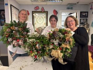 Three female veterans showing off their wreaths made during our Christmas wreath session