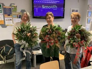 Three females holding wreaths made during a Christmas wreath making session