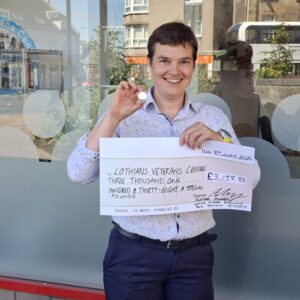 Dr Alethea McHardy holding a large cheque and gold pin badge