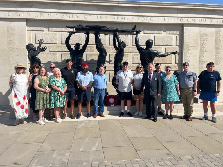 Group of male and female veterans standing in front of a memorial at the National Memorial Arboretum.